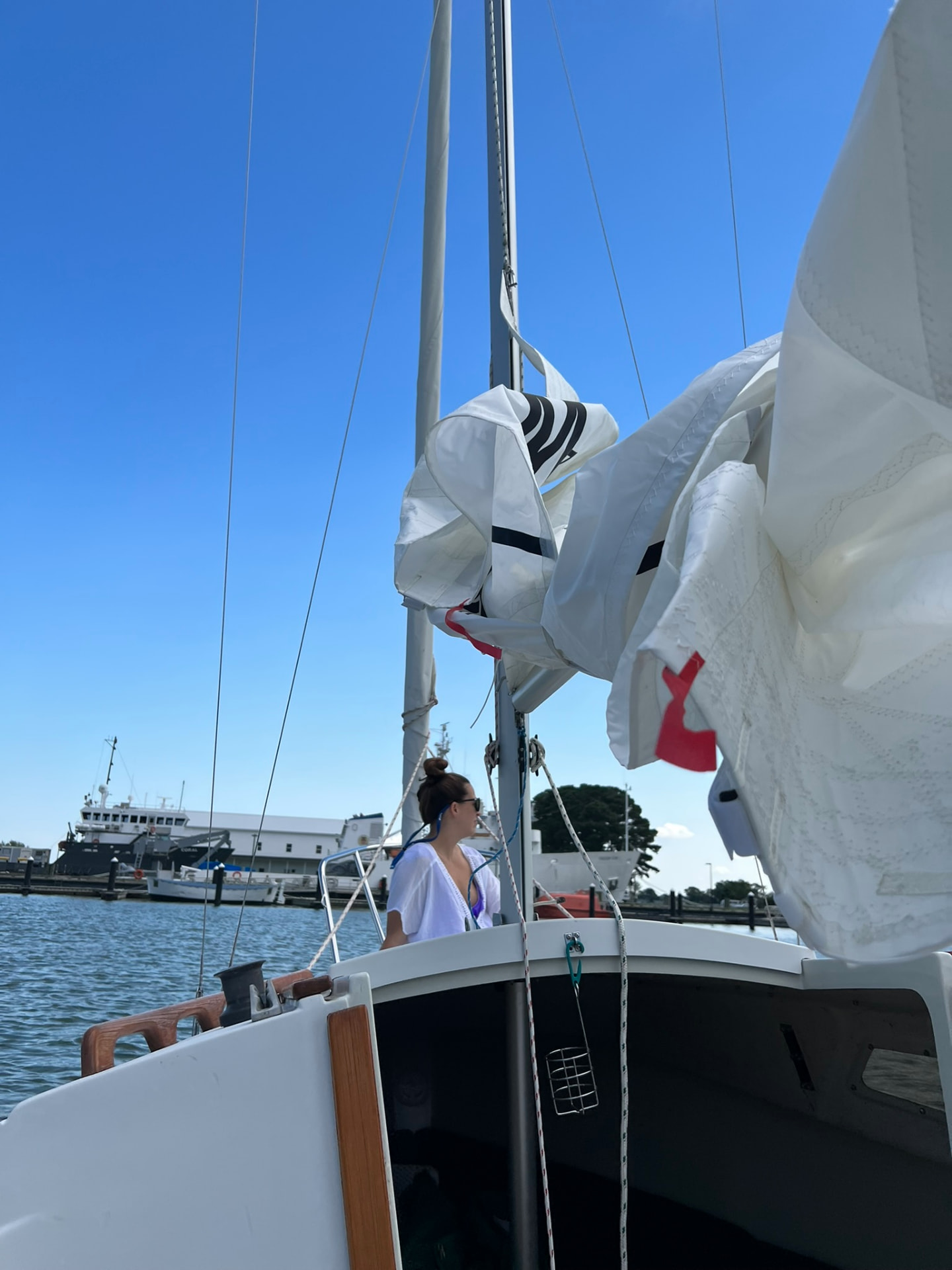 Sails flaked on the boom at the dock with a Navy vessel in the background