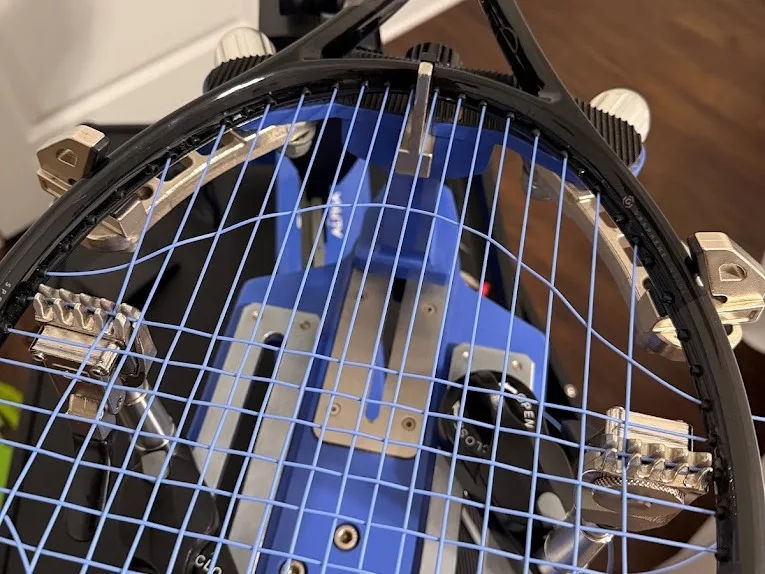 Tennis racquet mid-stringing with blue polyester string on a stringing machine at Birdman Strings in Odessa, FL