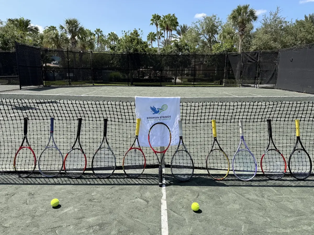 Customer tennis racquets lined up against a net with a Birdman Strings towel at a court in Pasco County, FL